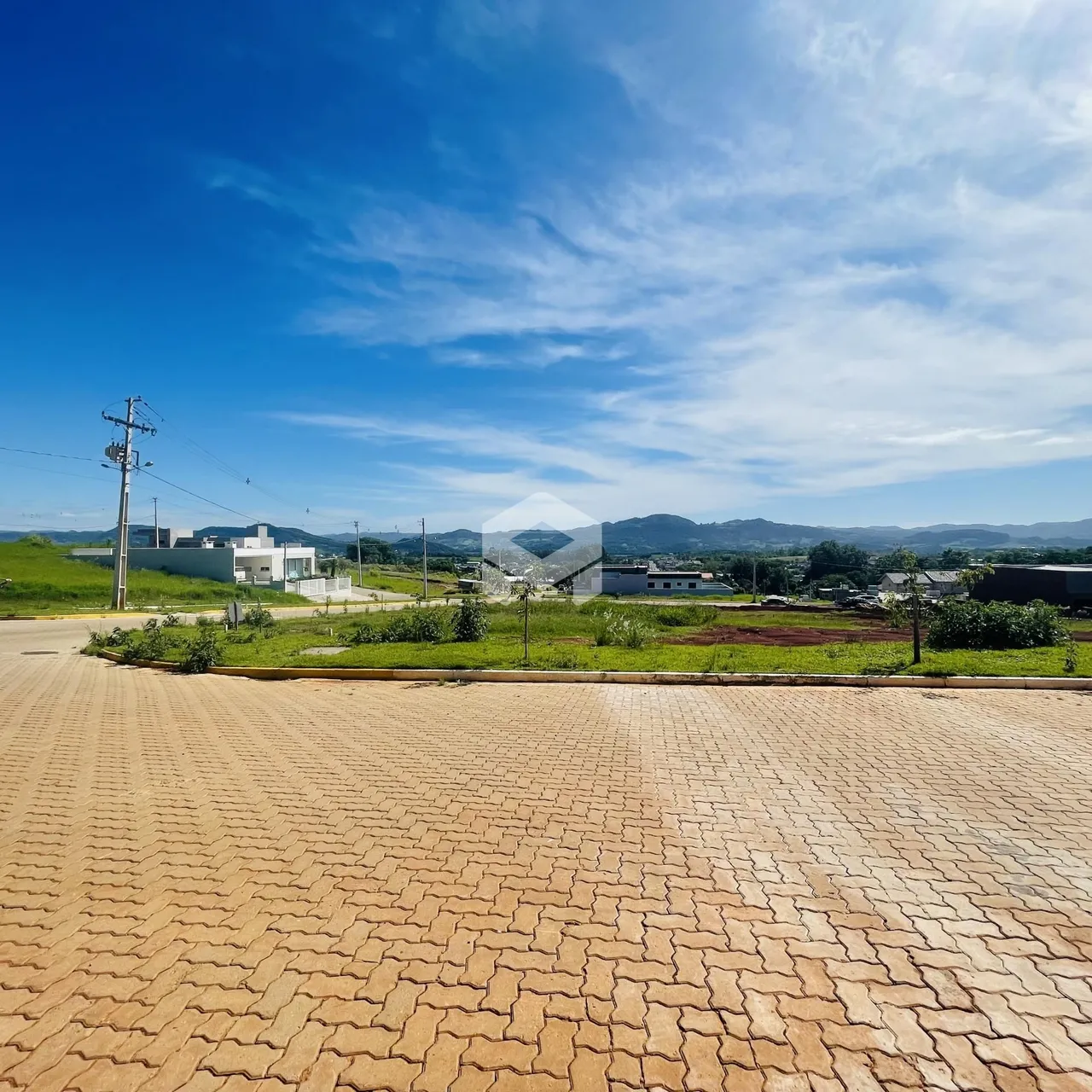 Vista externa de uma propriedade com área pavimentada e paisagem ao fundo.