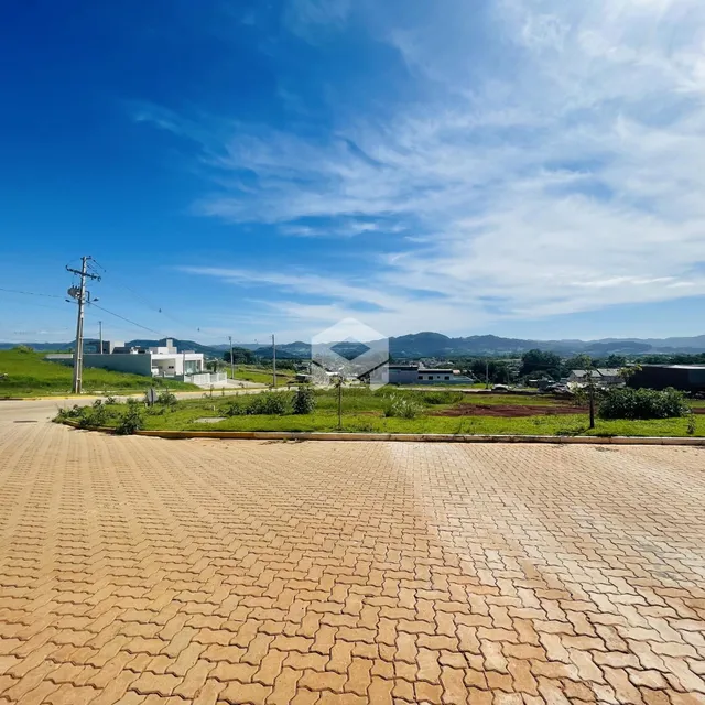Vista externa de uma propriedade com área pavimentada e paisagem ao fundo.