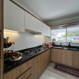 Cozinha com armários de madeira clara e bancadas escuras.