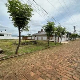 Vista externa de uma área com caminho de tijolos e vegetação em frente a um corpo d'água.