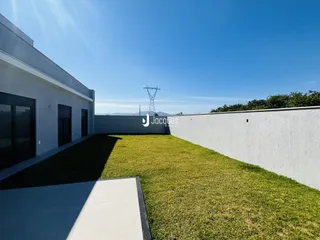 Fachada de uma residência branca com gramado verde e muro branco.