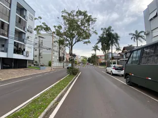 Vista de uma rua residencial em Lajeado, Brasil, com edifícios e árvores.