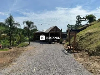 Vista externa de uma propriedade rural com estrada de cascalho e vegetação ao fundo.