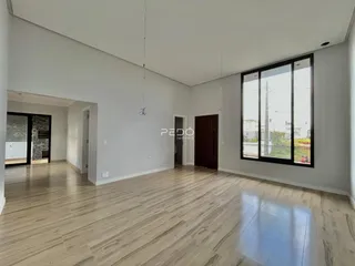 Ambiente interno de uma sala ampla com piso de madeira clara e grande janela.