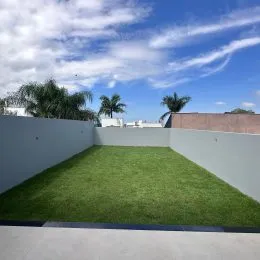 Vista de um gramado externo com muro branco e estrutura de alvenaria.