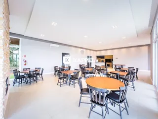 Imagem de um espaço comum com mesas e cadeiras em um ambiente interno claro.