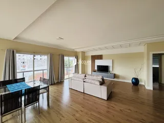 Uma sala de estar ampla com piso de madeira e grandes janelas.