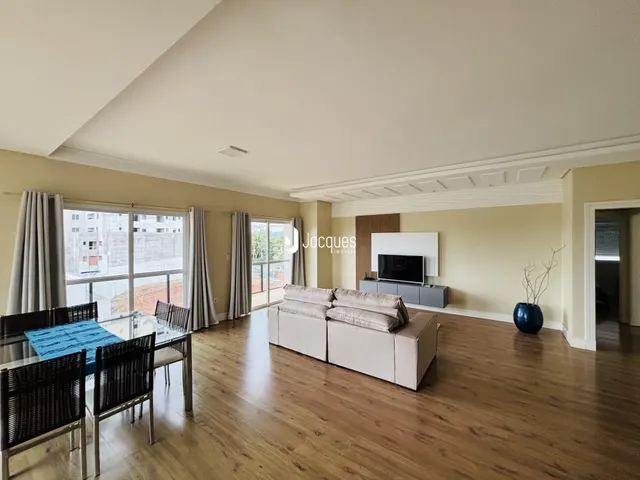Uma sala de estar ampla com piso de madeira e grandes janelas.