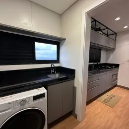 Foto interna da cozinha com armários escuros e bancadas escuras.