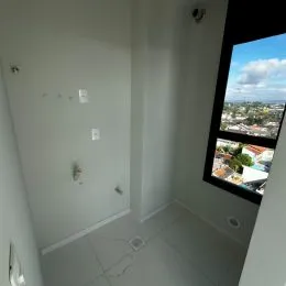 Hall de corredor interno com paredes brancas e uma janela com vista.