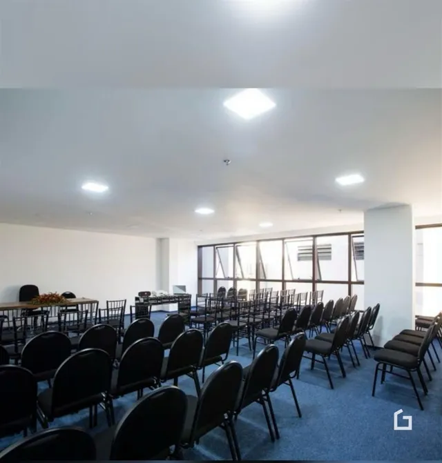 Uma sala grande está montada com mesas e cadeiras para um evento.