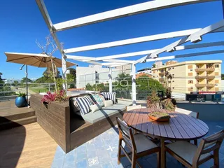 Vista de uma área de lazer externa com mobiliário de madeira e pérgola.