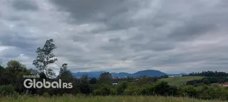 Paisagem de campo com montanhas ao fundo sob um céu nublado.