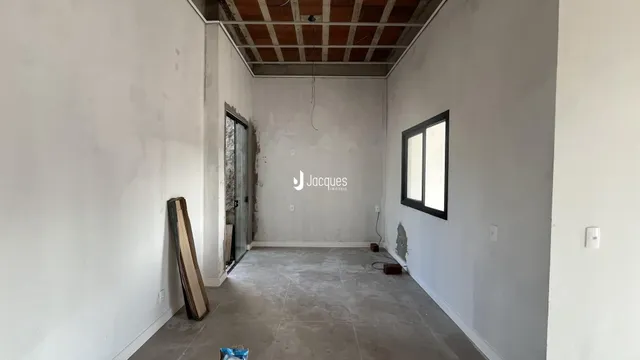 Interior de um espaço com paredes brancas e teto de estrutura exposta.