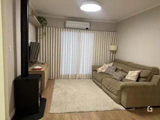 Sala de estar com sofá e janelas cobertas por cortinas claras.