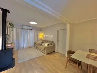 Sala de estar com piso de madeira clara e cortinas brancas.