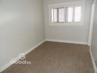 Vista interna de uma sala com paredes brancas e piso de madeira.