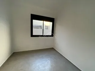 Vista interna de um cômodo com paredes brancas e uma grande janela.