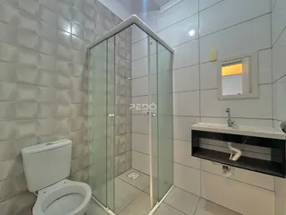 Foto interna de um banheiro com box de vidro e azulejos brancos.