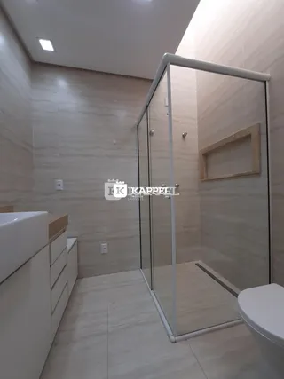 Banheiro com revestimento de azulejos claros e box de vidro transparente.