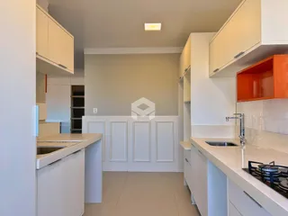 Vista interna de uma cozinha moderna com armários brancos e bancadas claras.