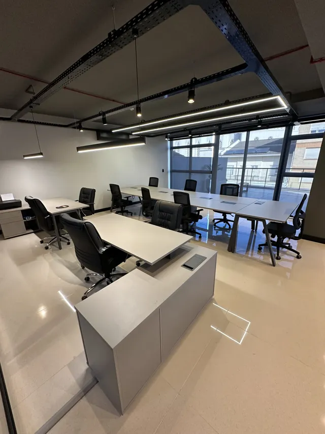 Ambiente de escritório moderno com mesas longas e cadeiras de trabalho.