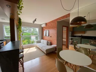 Sala de estar com sofá claro e grandes janelas com vista para o exterior.