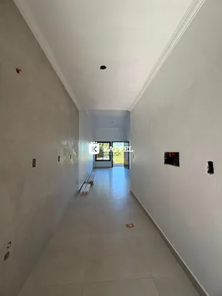Um corredor longo e estreito com paredes brancas e piso claro.