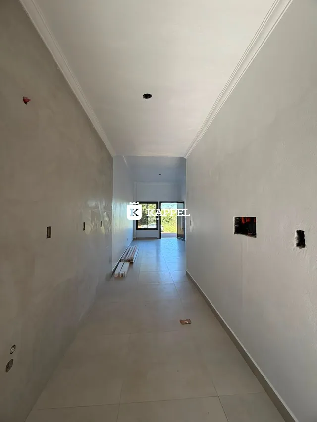 Um corredor longo e estreito com paredes brancas e piso claro.