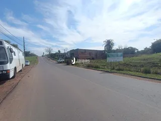 Vista de uma estrada rural com vegetação e construções ao fundo.