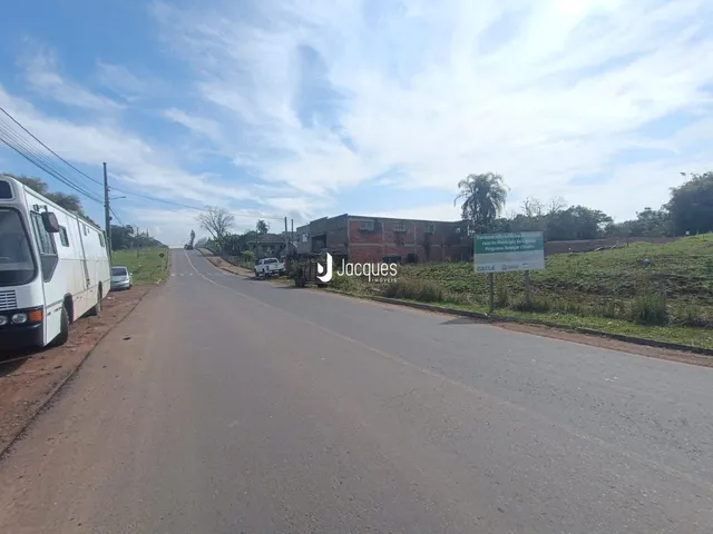 Vista de uma estrada rural com vegetação e construções ao fundo.
