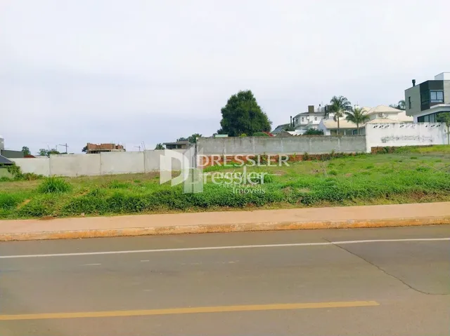 Vista externa de uma propriedade com gramado e muro ao lado de uma estrada.