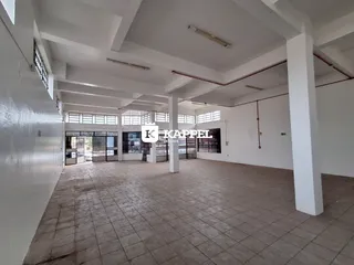 Vista interna de um espaço amplo com piso de cerâmica e estrutura de vigas expostas.