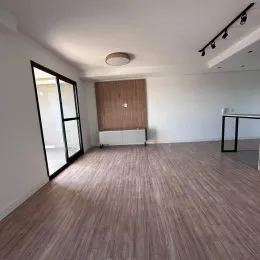 Sala de estar com piso de madeira e grandes janelas.