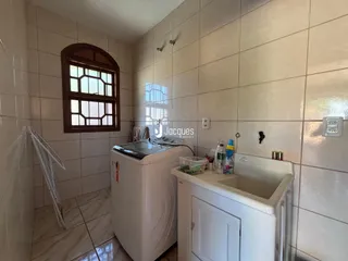 Imagem de um banheiro com azulejos brancos e máquina de lavar roupa.
