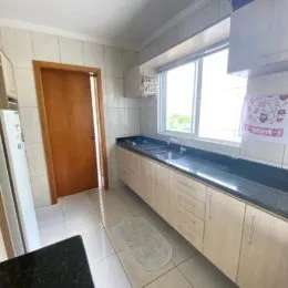 Vista interna de uma cozinha com armários e piso de cerâmica.