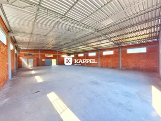 Foto interna de um espaço amplo com estrutura metálica e paredes de tijolo aparente.
