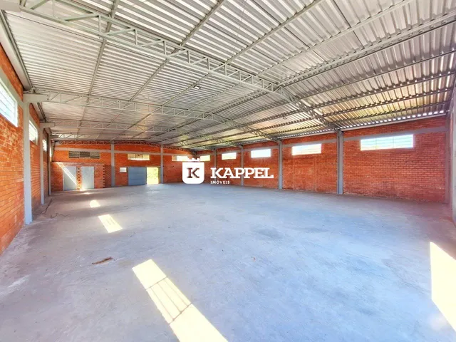 Foto interna de um espaço amplo com estrutura metálica e paredes de tijolo aparente.