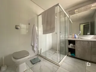 Banheiro com box de vidro e piso de cerâmica clara.