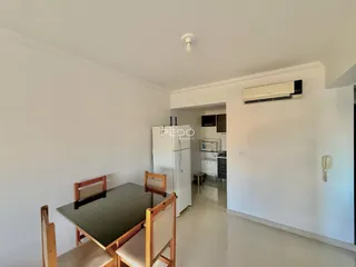Ambiente interno com mesa de jantar de madeira e paredes brancas.