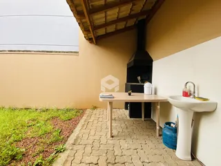 Vista externa de um pátio com piso de tijolos e vegetação ao lado de uma parede de cor bege.