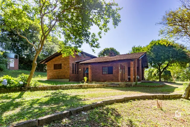 Fachada de casa de tijolos com jardim e vegetação ao redor.