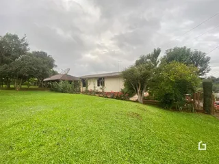 Vista externa de uma casa com gramado verde e vegetação ao redor.