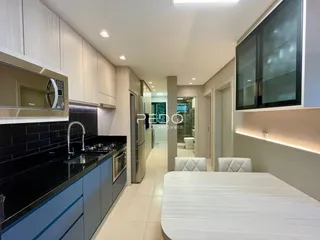 Vista interna de uma cozinha moderna com armários brancos e bancadas escuras.