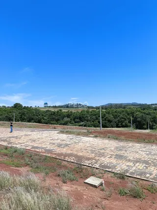 Paisagem de campo com terra vermelha e vegetação ao fundo.