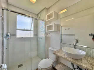 Banheiro com box de vidro e revestimento cerâmico nas paredes.
