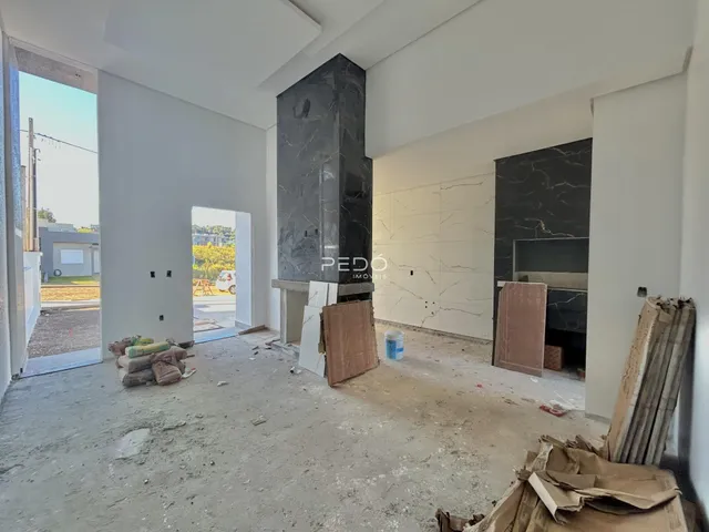 Interior de uma sala em construção com piso de concreto e paredes brancas.