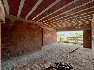 Imagem de uma sala em construção com paredes de tijolo aparente e teto de madeira.