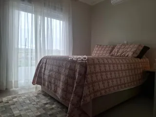 Quarto com cama e janela iluminada por cortinas brancas.