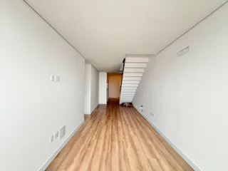 Foto de um corredor interno com piso de madeira e escadaria branca.